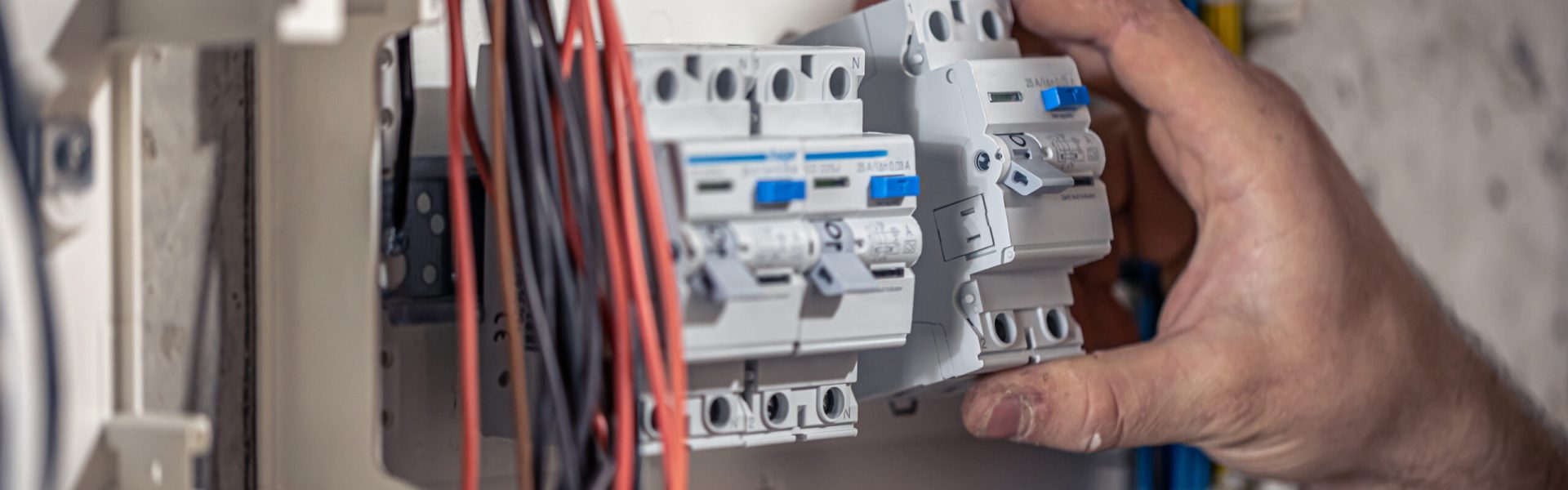 A male electrician works in a switchboard with an electrical connecting cable, connects the equipment with tools.