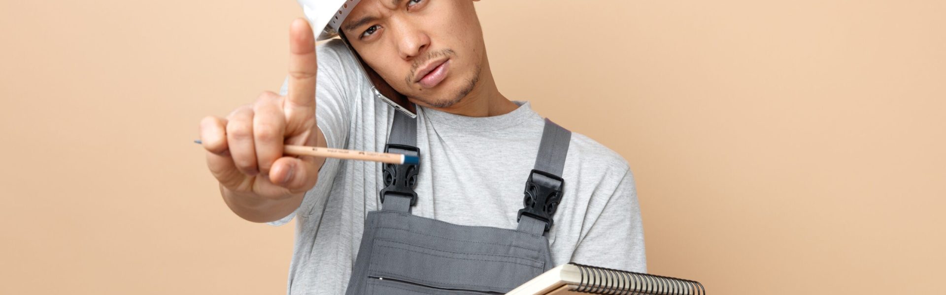 strict-young-construction-worker-wearing-safety-helmet-uniform-holding-notepad-pencil-doing-hold-gesture (1) (1)