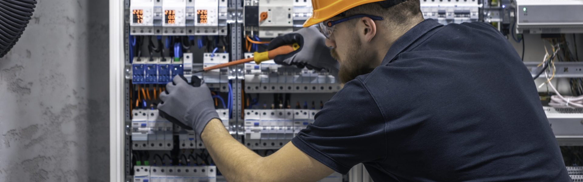 Young adult electrician civil engineer screwing equipment into fuse box.